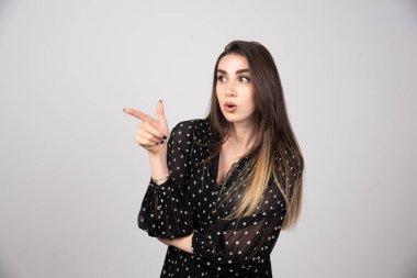 Gri bir duvarda parmağını gösteren sevimli genç bir kadın. Yüksek kalite fotoğraf