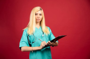 Sarı hemşire elinde panoyla kırmızı arka planda duruyor. Yüksek kalite fotoğraf