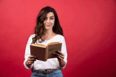 Kırmızı arka planda kitap okuyan genç bir kadın. Yüksek kalite fotoğraf