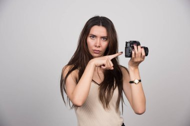 Gri arkaplandaki kamerayı gösteren genç bir kadın. Yüksek kalite fotoğraf