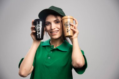 Kahve fincanlarıyla poz veren yeşil üniformalı teslimatçı kadın. Yüksek kalite fotoğraf