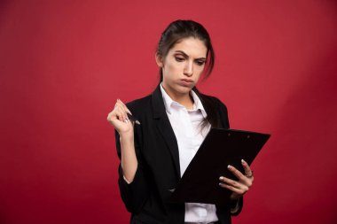 Genç iş kadını kırmızı arka planda ulaşılabilir tarihleri kontrol ediyor. Yüksek kalite fotoğraf