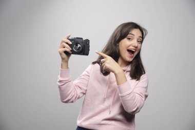 Gri bir duvarın üzerinde kamerayla poz veren güzel genç bir kadın. Yüksek kalite fotoğraf