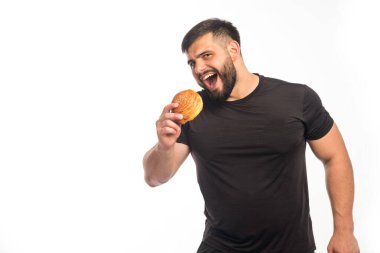 Siyah tişörtlü, elinde donut tutan ve yemek yiyen bir sporcu. Yüksek kalite fotoğraf