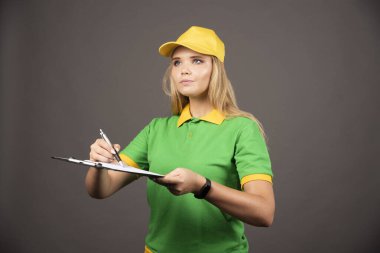 Kalem ve not panosuyla gözlerini kaçıran genç bayan kurye. Yüksek kalite fotoğraf