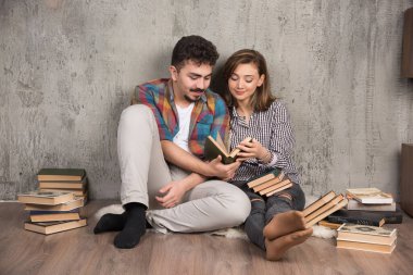 Yerde oturup kitap okuyan genç bir çiftin fotoğrafı. Yüksek kalite fotoğraf