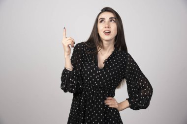 Gri bir duvarda parmağını gösteren sevimli genç bir kadın. Yüksek kalite fotoğraf