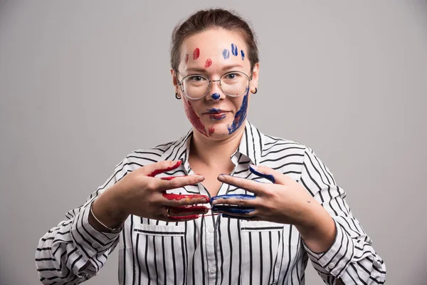 Yüzünde boya ve gri arka planda gözlük olan bir kadın. 