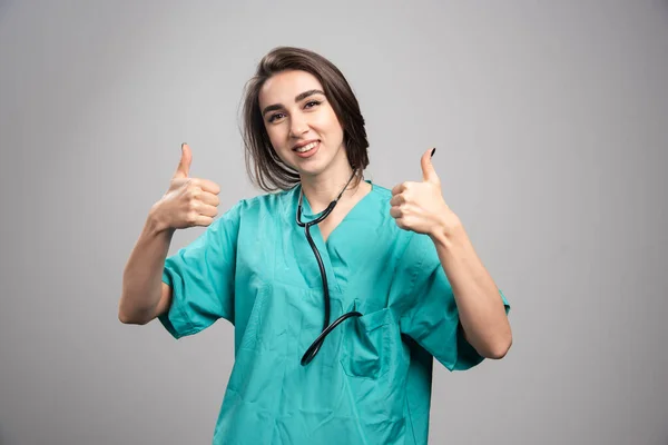 灰色の背景に親指をあきらめる制服の若い医者 高品質の写真 — ストック写真