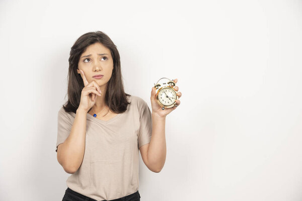 Молодая женщина держит будильник на белом фоне. Высокое качество фото