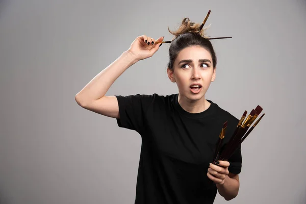 Beautiful woman with messy bun holding brushes. High quality photo