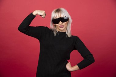 Kırmızı arka planda siyah gözlüklü, ayakta duran ve poz veren kadın portresi. Yüksek kaliteli fotoğraf.