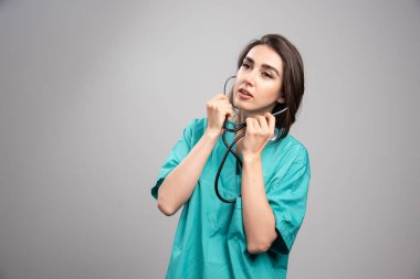 Üniformalı genç doktor gri arka planda steteskop kullanıyor. Yüksek kalite fotoğraf