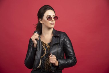 Siyah deri ceketli ve güneş gözlüklü havalı kız katı ve talepkar görünüyor. Yüksek kalite fotoğraf