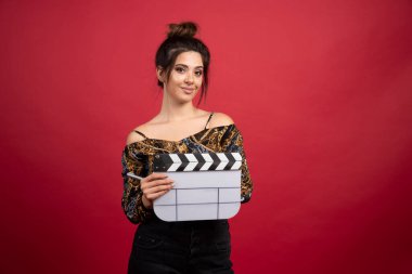 Esmer kız, kırmızı arka planda film yapımı için boş bir el çırpma tahtası tutuyor. Yüksek kalite fotoğraf