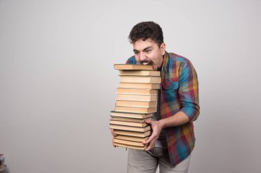 Genç adam gri bir duvarda bir sürü kitap tutuyor. Yüksek kalite fotoğraf
