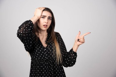 Gri bir duvarda parmağını gösteren sevimli genç bir kadın. Yüksek kalite fotoğraf