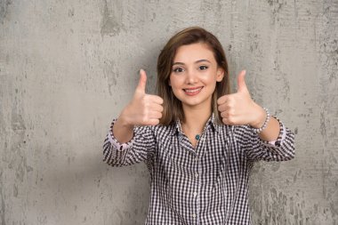 Karanlık arka planda izole edilmiş genç bir kadın iki eliyle baş parmağını kaldırıyor. Yüksek kalite fotoğraf