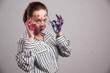 Yüzünde boya olan kadın gri arka planda gözlük takıyor. 