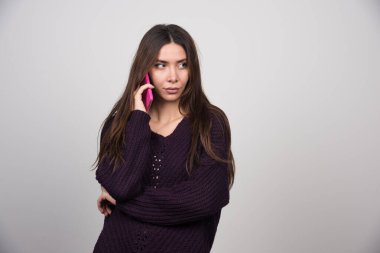 Pembe akıllı telefondan konuşan, kalın kazaklı genç bir kadın. Yüksek kalite fotoğraf