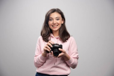 Gülümseyen fotoğrafçı gri arka planda kamera tutuyor. Yüksek kalite fotoğraf