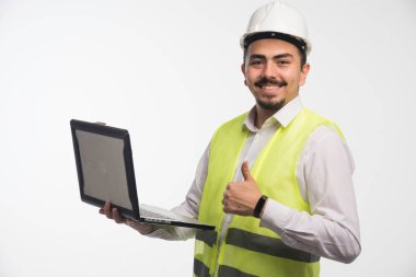 Üniformalı bir mühendis dizüstü bilgisayar tutuyor ve parmak kaldırıyor. Yüksek kalite fotoğraf