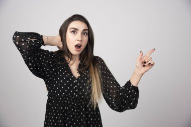 Gri bir duvarda parmağını gösteren sevimli genç bir kadın. Yüksek kalite fotoğraf