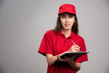 Kırmızı üniformalı teslimatçı kadın klipte yazıyor. Yüksek kalite fotoğraf