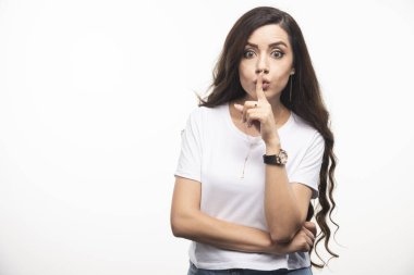 Beyaz gömlekli genç bir kadın beyaz arka planda sessiz işareti yapıyor. Yüksek kalite fotoğraf