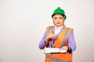 Beyaz arka planda yeşil miğferi ve panosu olan genç bir kadın müteahhit. Yüksek kalite fotoğraf