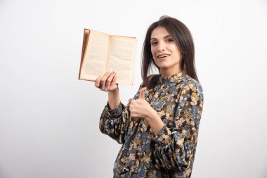 Esmer kadın bir kitap tutuyor ve başparmağını kaldırıyor. Yüksek kalite fotoğraf