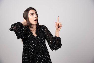 Gri bir duvarda parmağını gösteren sevimli genç bir kadın. Yüksek kalite fotoğraf