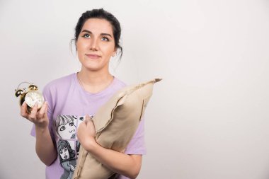 Üzgün kadın beyaz arka planda çalar saat ve yastıkla aşağı bakıyor.