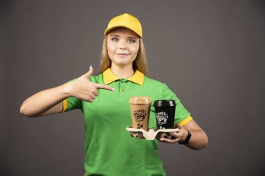 Genç teslimatçı kadın arka plandaki kahve fincanlarını işaret ediyor. Yüksek kalite fotoğraf