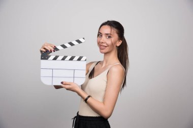 Gülümseyen kadın gri arka planda el çırpma tahtası tutuyor. Yüksek kalite fotoğraf