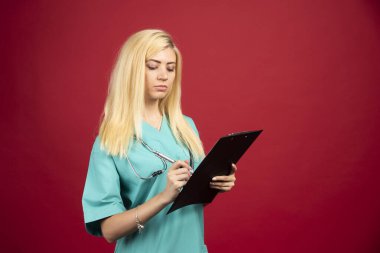 Ciddi bir hemşire kırmızı arka planda panosuna notlar yazıyor. Yüksek kalite fotoğraf