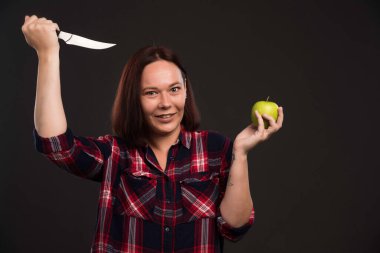 Sonbahar kış koleksiyonu giysileri içindeki kadın model yeşil bir elmanın üzerine bıçak koyuyor. Yüksek kalite fotoğraf