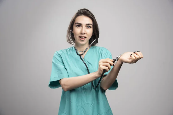 グレーの背景で自分自身をチェック聴診器を持つ女性医師 高品質の写真 — ストック写真