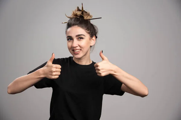 Young woman with messy bun giving thumbs up on gray background. High quality photo