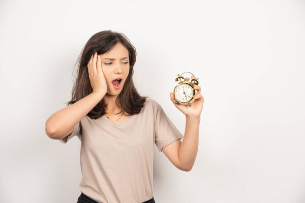 Шокированная женщина держит будильник на белом фоне. Высокое качество фото