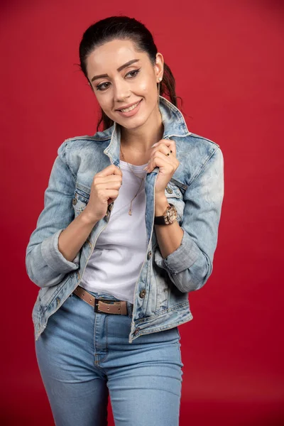 Positive woman in denim jacket standing on red background. High quality photo
