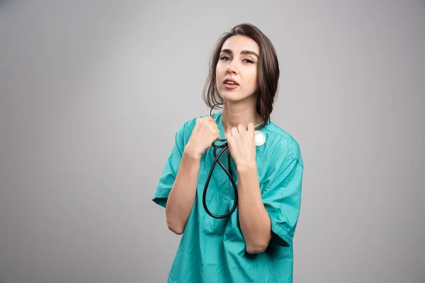 灰色の背景に聴診器を使用して均一で若い医師 高品質の写真 — ストック写真