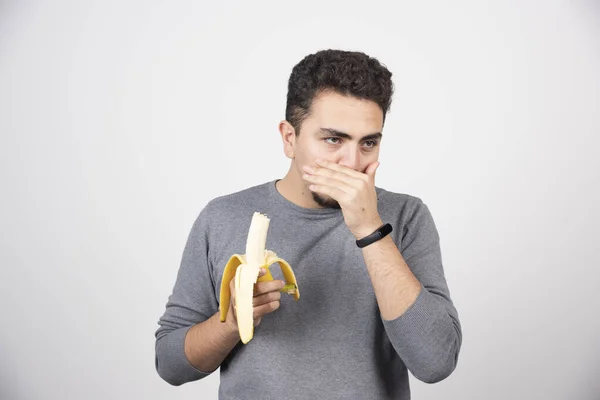 白い壁の上にバナナを食べる若い男 高品質の写真 — ストック写真