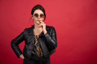 Siyah deri ceketli havalı kız parmağını çenesine dayayıp düşünüyor. Yüksek kalite fotoğraf