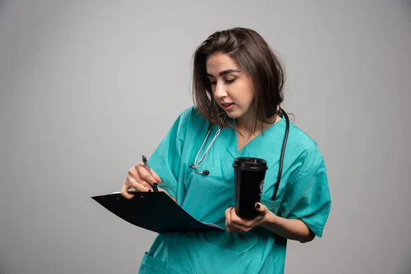 若い医者は灰色の背景の病気に関するメモをチェックする 高品質の写真 — ストック写真