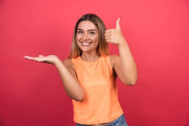 Güzel genç bayan kırmızı arka planda başparmak kaldırıyor. Yüksek kalite fotoğraf