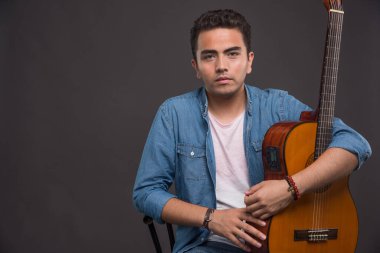 Gitarlı genç adam karanlık arka planda ciddi görünüyor. Yüksek kalite fotoğraf