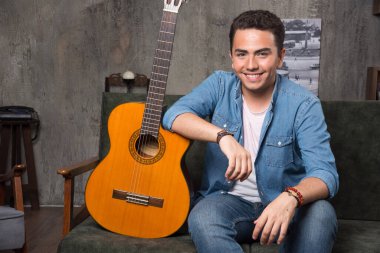 Gülümseyen gitarist elinde güzel bir gitaristle kanepede oturuyor. Yüksek kalite fotoğraf