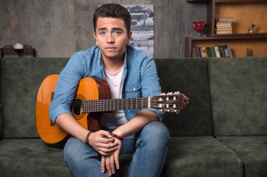 Genç gitarist elinde güzel bir gitaristle kanepede oturuyor. Yüksek kalite fotoğraf