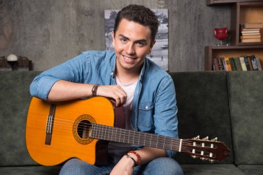 Elinde güzel bir gitarla kanepede oturan pozitif bir adam. Yüksek kalite fotoğraf